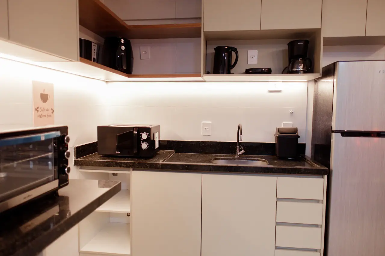 Cozinha com bancada escura, geladeira e luz sob os armários