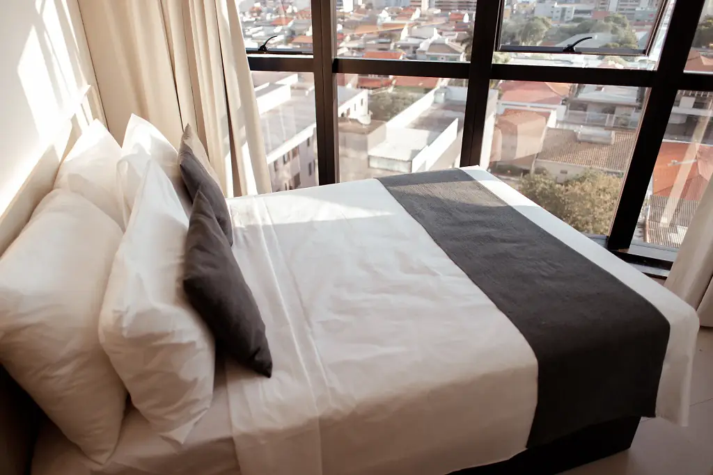 Cama de casal arrumada junto à janela com vista da cidade